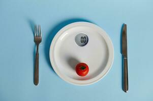 cuchillería y tomate en un plato en el formar de medición escamas, aislado en azul antecedentes con Copiar espacio foto