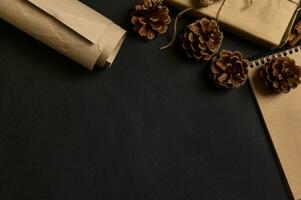 Black background with pine cones , cropped Christmas gift in craft wrapping paper in the corner of the image photo