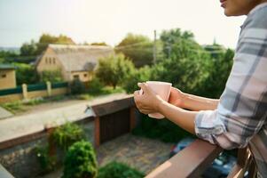 Focus on female hands holding cup of hot drink, on the balcony photo