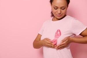 Close-up, mixed race woman puts hands under pink ribbon on her pink T Shirt, for breast cancer campaign, supporting Breast Cancer Awareness. Concept of 1 st October Pink Month and women's health care photo