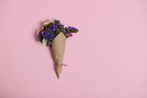 Flat lay of floral composition of beautiful meadow flowers wrapped in wrapping craft paper tied with rope, isolated on pink background with copy space. photo