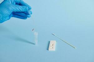 A hand in a medical glove holds a medical disposable pipette for taking a sample for express test for covid antigen photo