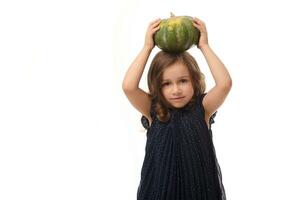 Halloween Witch concept. Waist-length shot of little European girl dressed in stylish carnival attire and wizard hat, witch child posing with pumpkin on her head against a white background, copy space photo