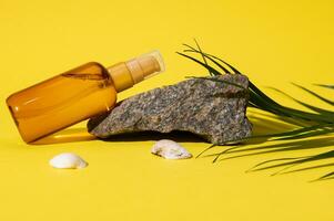 Unbranded cosmetic mockup bottle of sunscreen soothing body oil displayed on a small rock near sea shells. UV protection photo