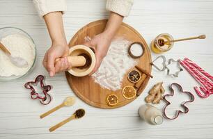 Top view of woman's hands grinding spices and ingredients in a marble mortar, while preparing Christmas cookies in the kitchen table photo