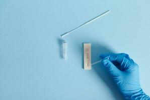 A hand in a protective medical glove drips a reagent into a test strip and does a covid-19 rapid antigen test on a blue background photo