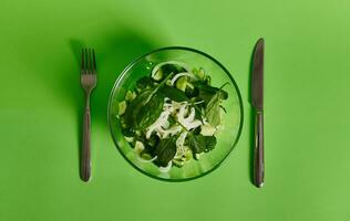 Flat lay of a fork and knife near a plate of green salad on green background photo