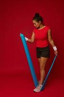 Full length of a sporty woman using elastic fitness rubber band exercises against red background with copy space for advertisement text. Fitness, sport, active and healthy lifestyle concept photo