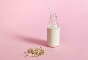 Close-up view of glass bottle with milk and oat flakes on pink background with space for text photo