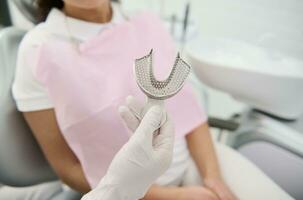 Close-up of a dentist's hand holding Dental mold dentists teeth ceramic plate cast on the background of a patient sitting in the dentist's chair at dentistry clinic photo