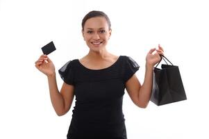 aislado retrato en blanco antecedentes con Copiar espacio de atractivo sonriente mujer vestido en negro y participación un descuento crédito tarjeta y un compras bolsa, mirando a cámara. negro viernes concepto foto