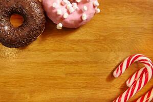 Assorted doughnuts with sprinkles and Christmas candy cane on a wooden surface. Background with copy space. photo