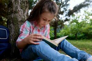 de cerca retrato de un Chica de escuela leyendo un libro en el parque. infancia. aficiones y ocios educación. inteligente niños foto