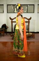 un tradicional indonesio bailarín en pie en un amarillo disfraz y un naranja bufanda colgando abajo su cuerpo foto