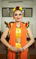 a traditional Indonesian dancer standing in a yellow costume and an orange scarf hanging down her body photo