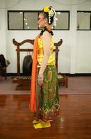 a traditional Indonesian dancer standing in a yellow costume and an orange scarf hanging down her body photo