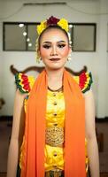 un tradicional indonesio bailarín en pie en un amarillo disfraz y un naranja bufanda colgando abajo su cuerpo foto