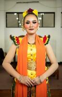 a traditional Indonesian dancer standing in a yellow costume and an orange scarf hanging down her body photo