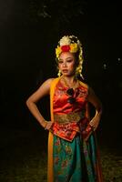 a Javanese dancer poses with sharp eyes and a golden costume on stage photo