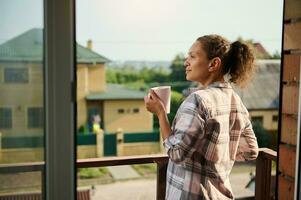 Hispanic pretty woman with a cup of hot drink on balcony of her country house photo
