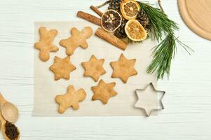 Gingerbread cookies as stars shape for Christmas, on a parchment paper with pine cones and branches, dried slices of orange and cinnamon sticks photo