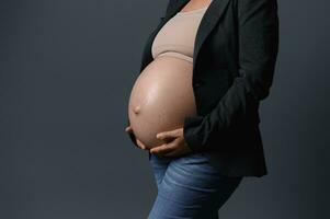 Close-up of beautiful pregnant belly in pregnancy 36 week, isolated gray studio background. Copy ad space. Childbearing photo