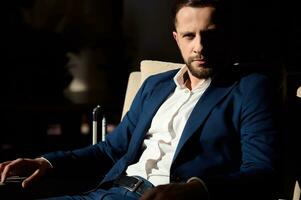 Attractive self-confident business traveler, handsome successful businessman, entrepreneur resting in an armchair in hotel lobby and confidently looking at camera photo