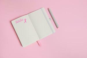 Lettering 1 st October on a diary and a pink ribbon on an empty blank paper sheet, isolated on pink background with copy space photo
