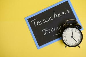 Flat lay composition from an alarm clock and chalkboard on yellow background with space for text. Teacher's Day photo