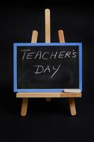 Close-up of a chalk board on a wooden table easel with lettering Teacher's Day , isolated on black background with copy space. photo