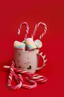 Christmas composition with hot chocolate decorated with marshmellows and candy canes isolated over red colored backgroud with copy space for ad photo