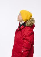 Isolated side portrait of a handsome child, adorable preteen school boy in bright yellow woolen hat and red down jacket with snow-covered hood looking in front of him on copy space of white background photo