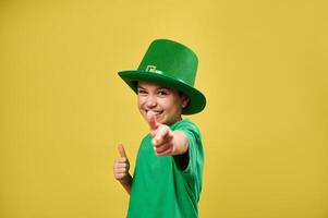 Happy boy pointing finger gun and showing thumb up to camera isolated on yellow background. Saint Patrick's Day. Copy space photo