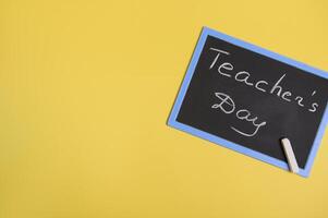 Flat lay of a chalckboard with inscription Teachers Day on a yellow background with copy space for text photo