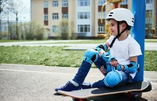 Cute child boy relaxed sitting on skateboard against yellow building background photo
