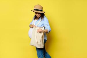 encantador embarazada mujer utilizando lino compras bolsa, aislado amarillo antecedentes con Copiar anuncio espacio. sostenible estilo de vida foto