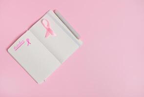 Lettering 1 st October on a diary and a pink ribbon on an empty blank paper sheet, isolated on pink background with copy space. Breast Cancer Awareness Month photo