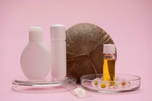 Mockup bottles on Petri dish with chamomile flowers, a smear of moisturizer on labglass and coconut on pink background. photo