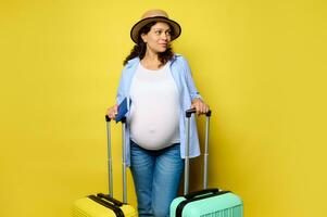 Charming pregnant woman travelling abroad, going for weekend getaway, looking aside a copy space on yellow background. photo
