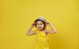 Beautiful little girl wearing summer hat poses on a yellow background with copy space expressing emotion, surprise photo