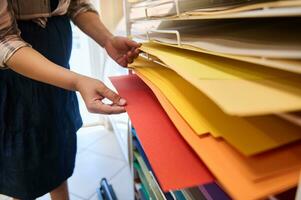 Close-up woman, customer in creative art store, choosing design cardboard sheets on shelves with colorful vibrant papers photo