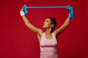 Pleasant active woman doing bodyweight training with resistance rubber band on red background with copy space for ads photo