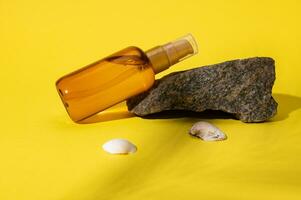 Unbranded cosmetic mockup bottle of sunscreen soothing body oil displayed on a small rock near sea shells. UV protection photo