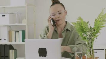 une femme dans des lunettes parlant sur le téléphone tandis que séance à une bureau video
