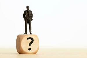 Figurine businessman on top of a wooden block with Question mark. Business question doubt. Copy space photo