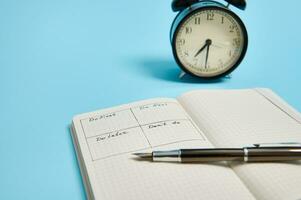 Time management, deadline concept. An open organizer notebook with timetable of the day by hour, ink pen, alarm clock on color background, copy space. Cropped image photo