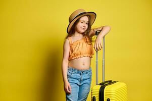 Happy little kid girl going for vacations, travelling abroad, winking and smiling looking at camera, isolated on yellow photo