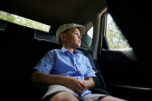 Teenage boy sitting in the rear passenger seat car and looking out the window photo