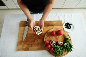 Top view of sliced mushroom in female chef hands. Ingredients for pizza filling on a wooden board in the home kitchen photo