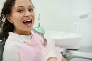 Close-up of dentist hand removing dental impressions of the upper jaw made of silicone material of a woman patient sitting in dentists chair. Dental molds . Imprint of the tooth row of high precision. photo